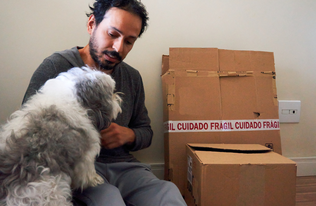 Man sitting on the floor with his dog next to cardboard boxes labeled fragile.