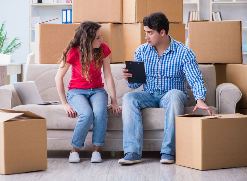 Man sitting on the couch with a woman discussing something on a clipboard.