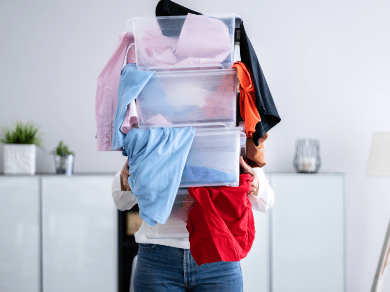 Person carrying plastic containers filled with clothes.